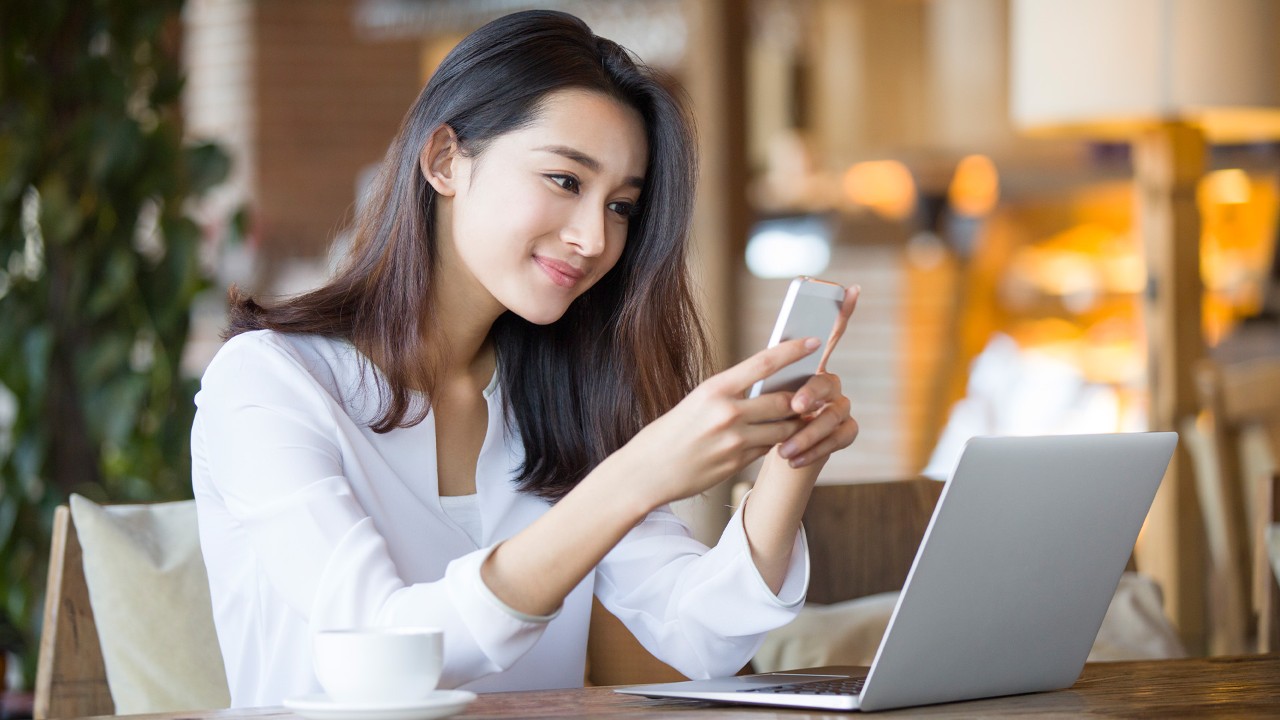 Girl holding mobile phone in coffee shop; image used for live within your means