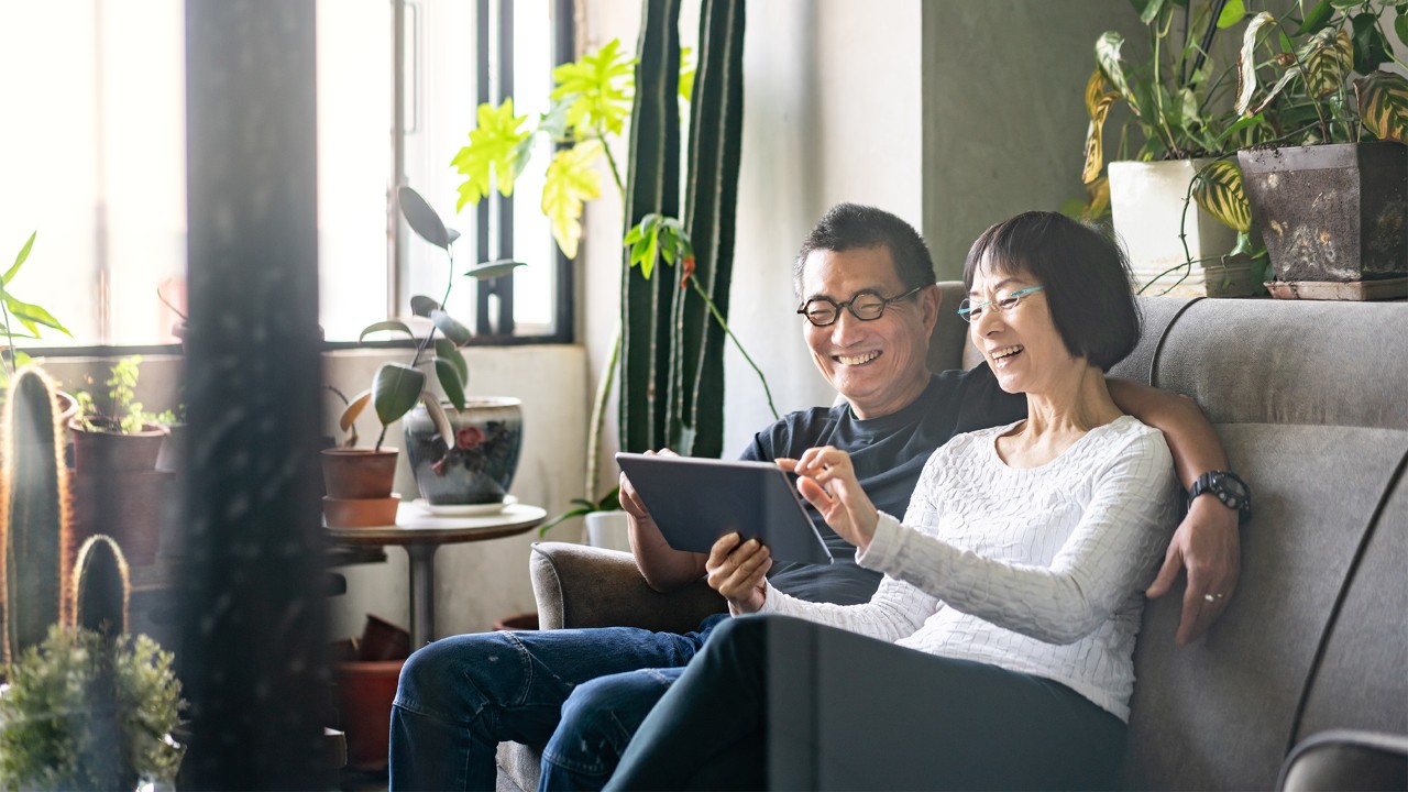 Middle-aged couple sitting on sofa looking at tablet; the image used for save for the future 