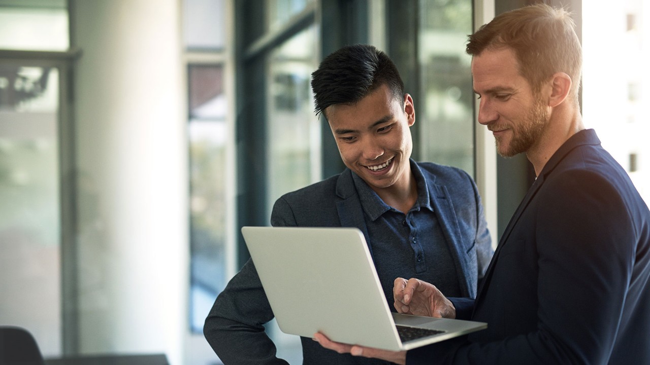 two men look at laptop; the image used for Overseas Investment Plan
