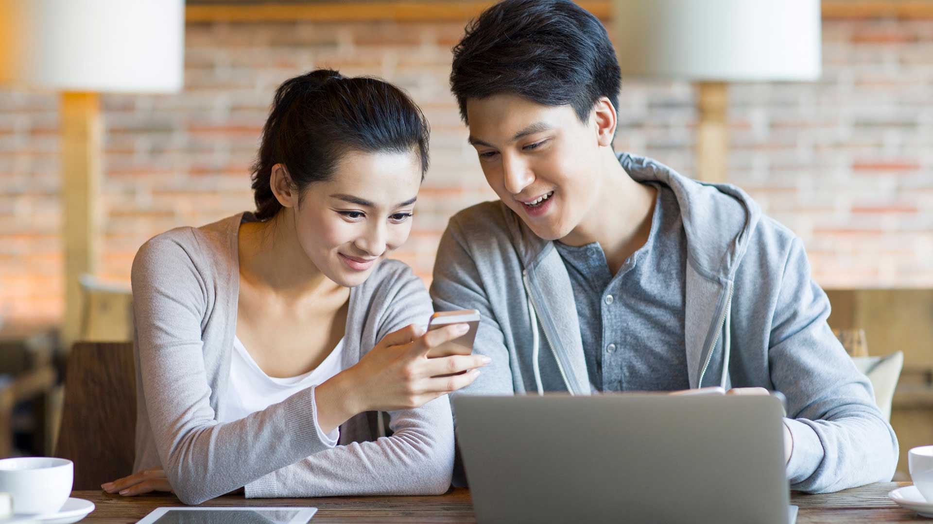 Young couple looking at mobile phone in front of computer; the image used for types of savings