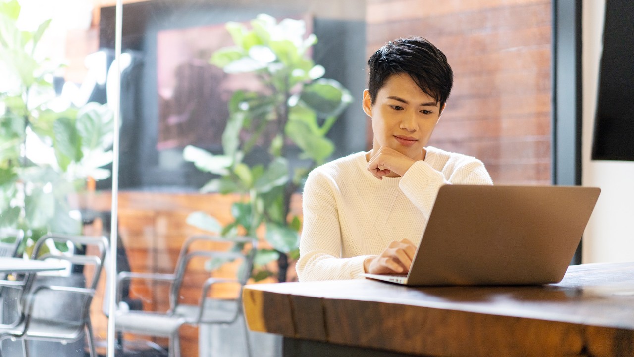Man looking at computer on balcony; the image used for beware of scams and fraud