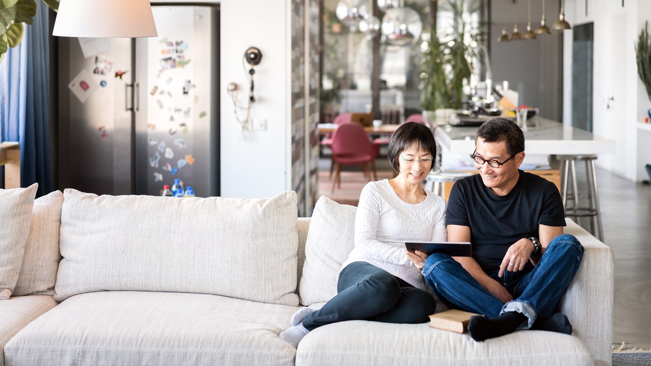 Middle-aged couple sitting on sofa looking at tablet; the image used for save for the future